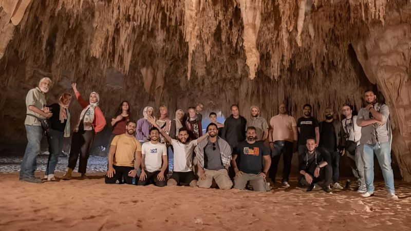 A group of travelers posing inside a large cave with impressive stalactites hanging from the ceiling