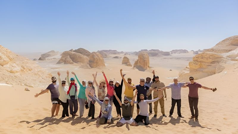 A group of people standing together with arms raised, surrounded by a scenic desert landscape