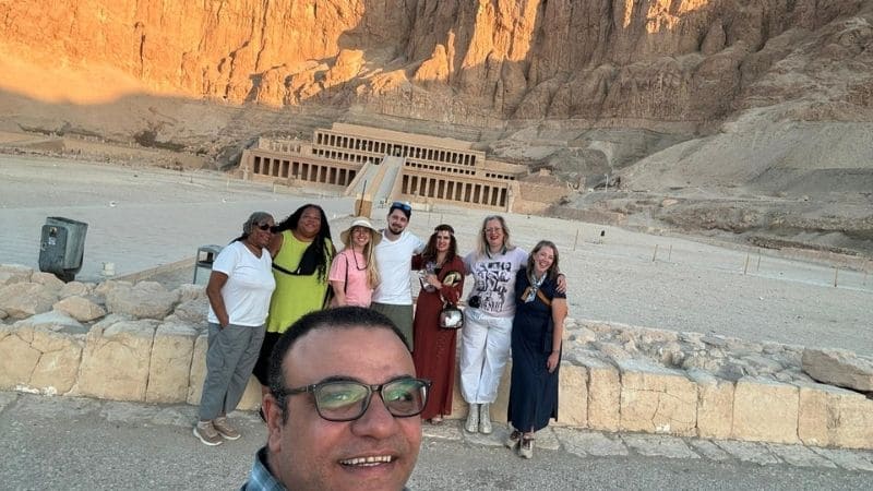 A tour group posing in front of the Temple of Hatshepsut in Luxor, Egypt, with the cliffside in the background