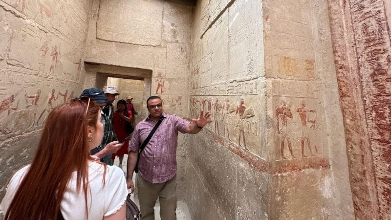 Tour guide explaining ancient Egyptian tomb carvings to visitors inside a historical site