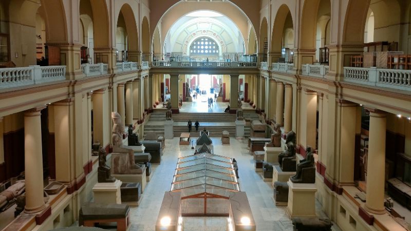 The interior of the Egyptian Museum in Cairo, featuring grand arches, stone statues, and displays of ancient artifacts under natural light.