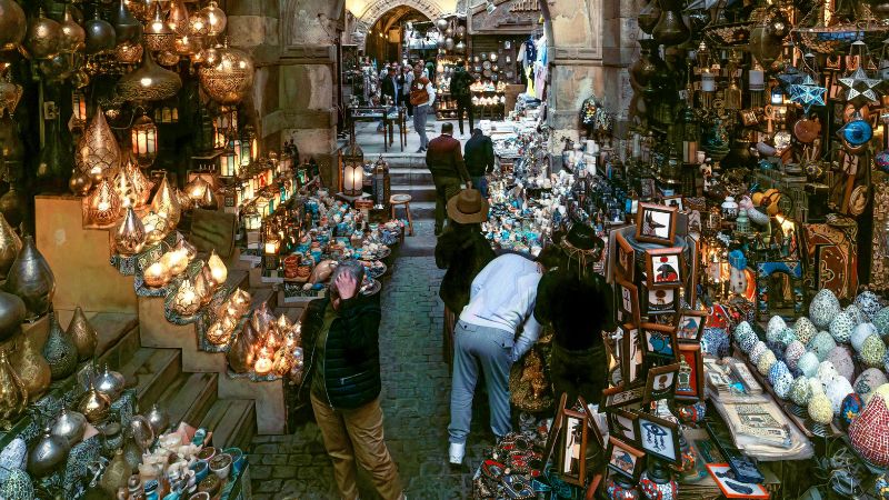 A bustling alley in Cairo's Khan El Khalili bazaar, filled with colorful lamps, handcrafted souvenirs, and shoppers exploring the vibrant marketplace