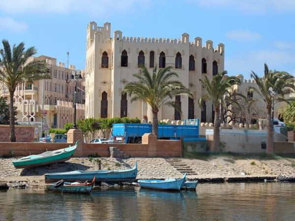 A quaint town by the Nile River, with traditional buildings, palm trees, and small wooden boats on the water