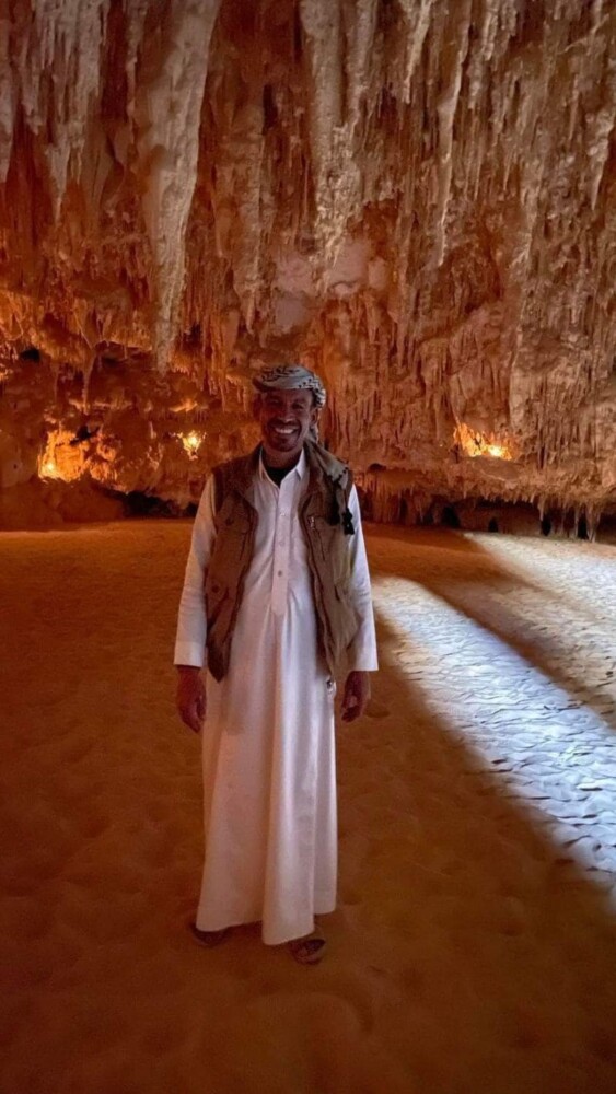 A man smiling inside a cave surrounded by stalactites and sand