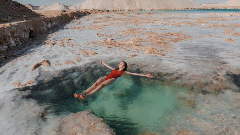 Woman floating in a crystal-clear salt pool surrounded by desert terrain