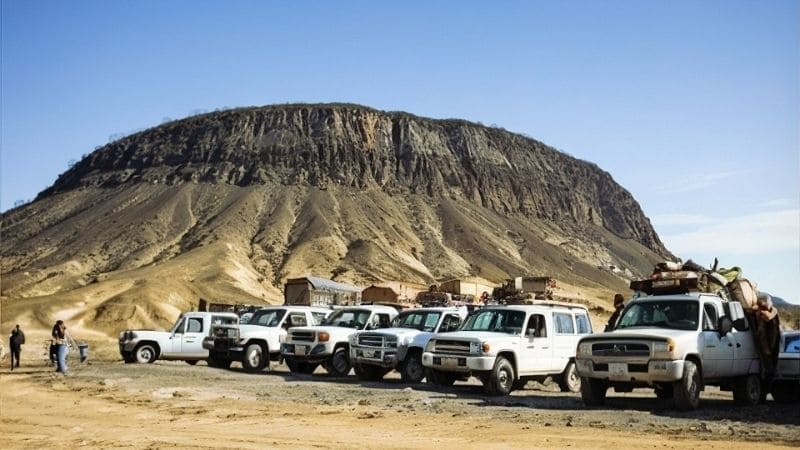 An off-road vehicle kicks up sand as it traverses Egypt's vast desert landscape under a clear blue sky