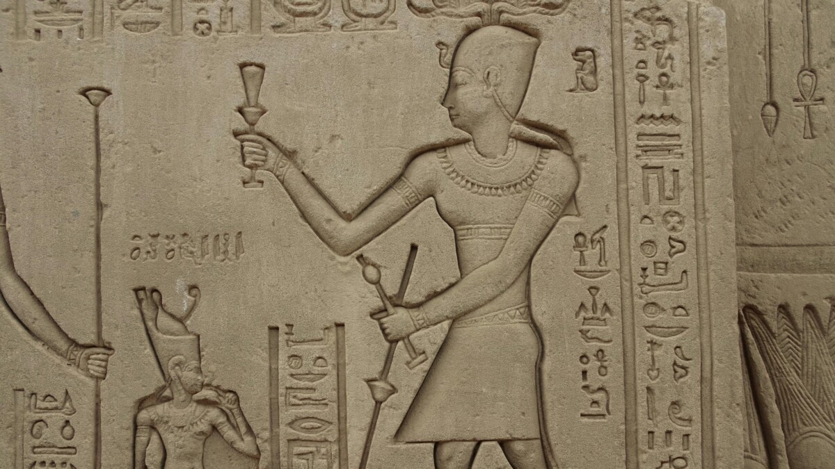 Wall relief of a pharaoh offering a ritual item in the Temple of Hathor, with intricate hieroglyphs in the background