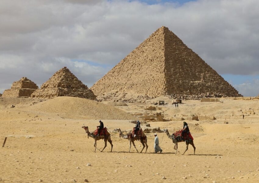 The majestic Pyramids of Giza under a bright blue sky, surrounded by desert sands