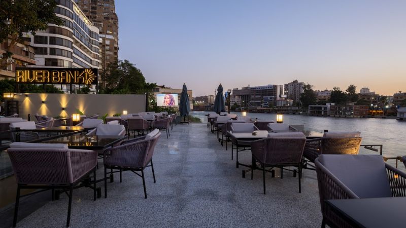 Outdoor restaurant with modern seating along the Nile River at sunset, surrounded by city buildings