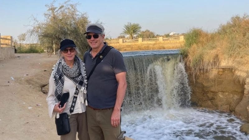 A serene view of travelers relaxing near an oasis waterfall in Egypt, surrounded by lush greenery and desert landscapes