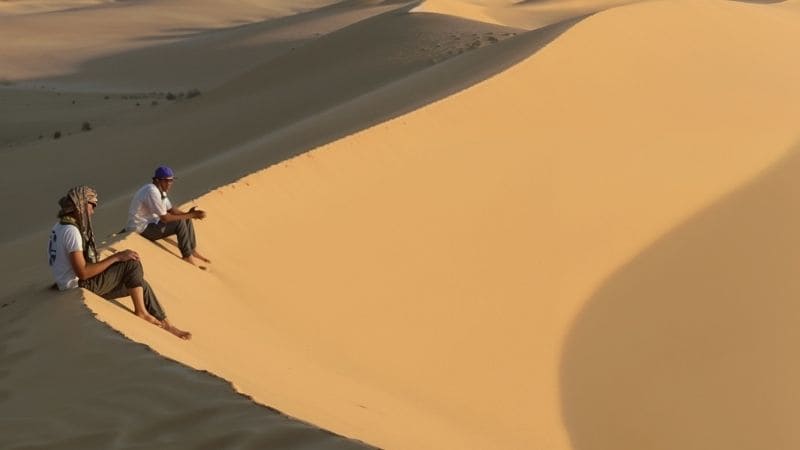 A traveler resting atop golden sand dunes under a clear blue sky in Egypt’s desert