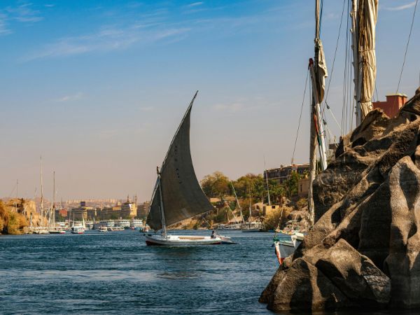 A traditional sailboat, or felucca, gliding along the Nile River near Aswan with rocky shores and palm trees