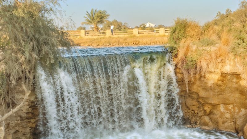 A picturesque view of a small waterfall surrounded by lush greenery in an Egyptian oasis