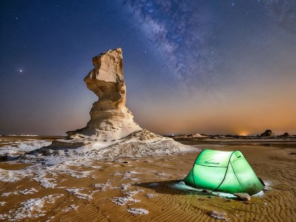 A tent illuminated under the Milky Way in Egypt’s White Desert, next to a unique rock formation