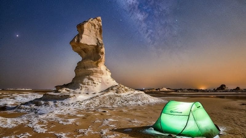 Green tent pitched under a rock formation in Egypt’s White Desert at night