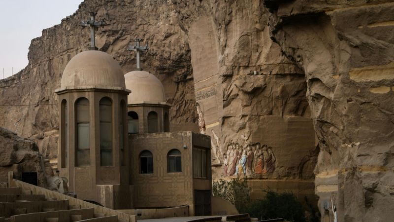 A stone church with cross-topped domes surrounded by carved religious artwork on a cliff