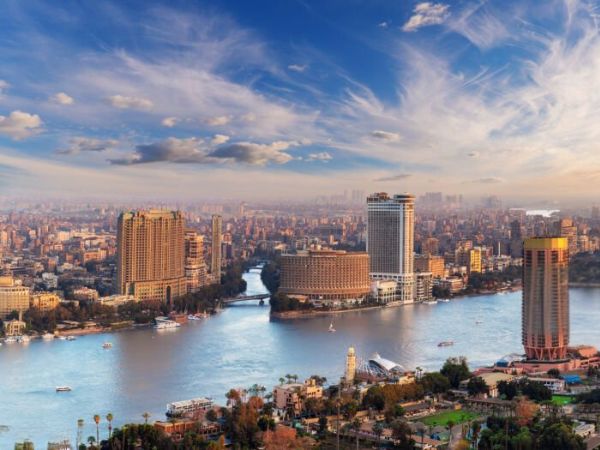 The bustling skyline of Cairo with modern high-rise buildings, the Nile River, and a vibrant urban atmosphere under a clear blue sky