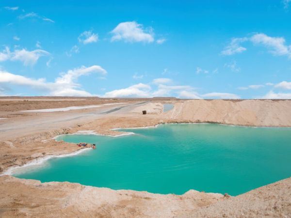 A vivid turquoise salt lake surrounded by desert landscapes under a blue sky