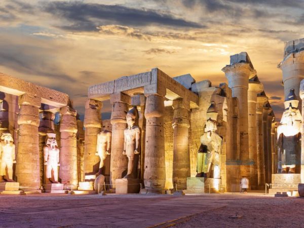 The illuminated Luxor Temple at night, with towering statues and columns glowing under a dramatic sky