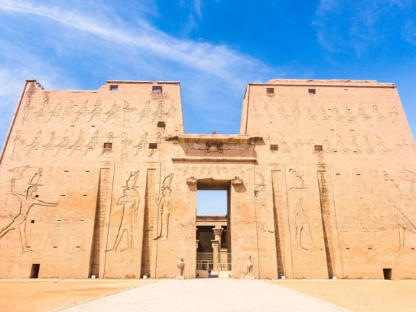 The grand entrance of Edfu Temple with intricate carvings on its walls and a bright blue sky overhead