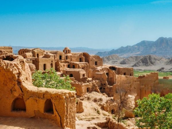 Ruins of an ancient desert village with clay structures and mountain views in the background