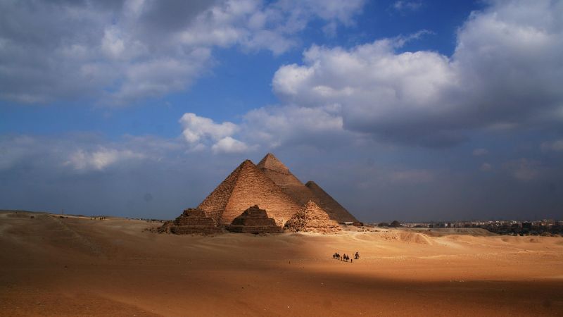 A wide-angle view of the Pyramids of Giza, with the iconic Great Pyramid and smaller pyramids standing under a dramatic sky