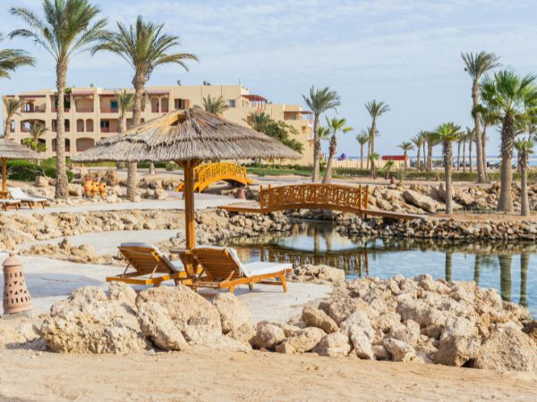 A scenic beach in Safaga with golden sands, palm trees, and a charming wooden bridge over calm waters