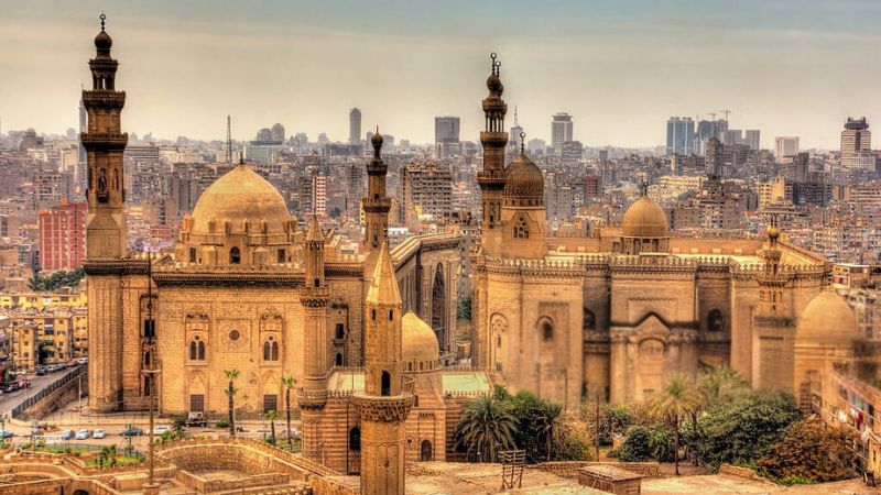 The Mosque of Sultan Hassan and the Al-Rifa'i Mosque in Cairo, with their grand domes and minarets standing against the backdrop of a bustling cityscape