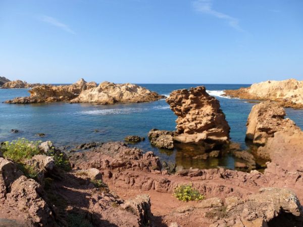 A rugged coastline with rocky outcrops extending into the blue waters of the sea under a clear sky