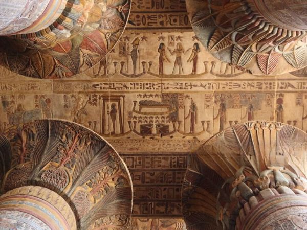 A richly decorated ceiling in an ancient Egyptian temple, with vivid colors and intricate carvings on the columns and panels