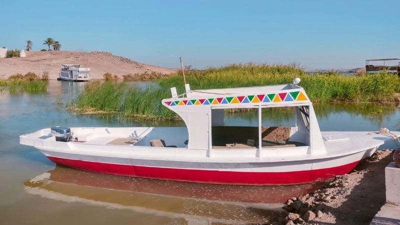 A colorful wooden boat docked by a calm river in Egypt, with reeds and another boat in the background