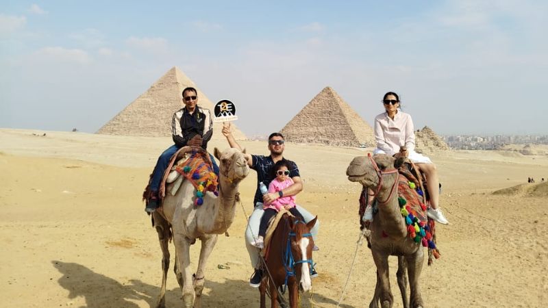 Tourists riding camels in front of the Great Pyramids of Giza on a sunny day