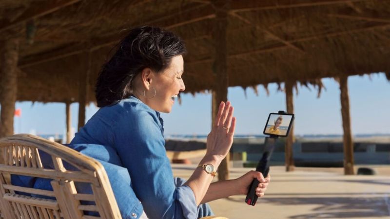 Woman video calling using a smartphone while seated at a beachside location