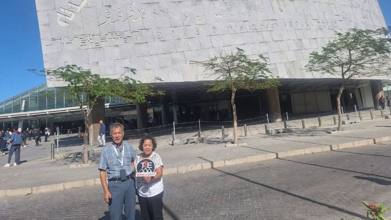 Tourists holding a Travel 2 Egypt sign in front of the modern Bibliotheca Alexandrina building in Alexandria, Egypt