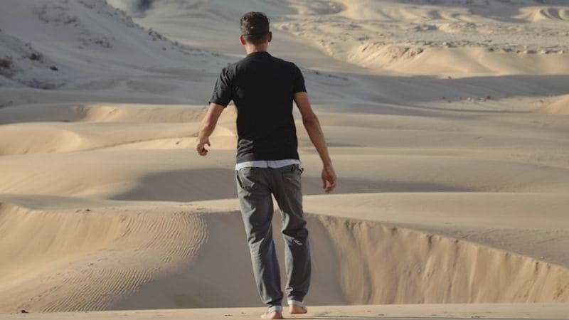 A person walking barefoot across Egypt's rolling sand dunes during daylight