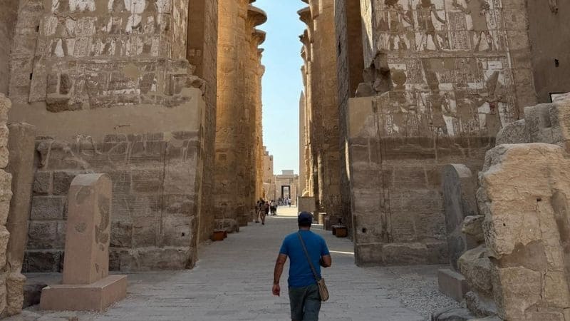 A man walking through towering stone columns decorated with hieroglyphics at Karnak Temple