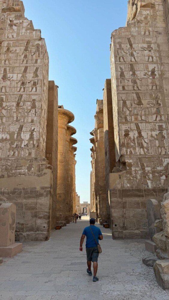 A tourist walking through towering, decorated stone columns at Karnak Temple in Egypt