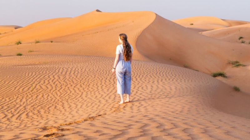 Woman walking barefoot on golden sand dunes in the desert