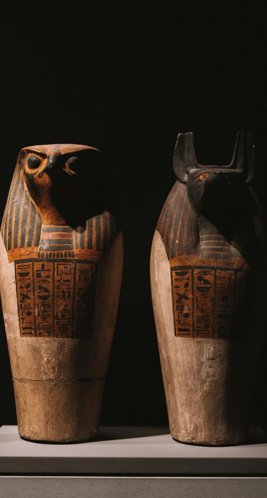 Two decorated canopic jars displayed in a museum exhibit against a dark background