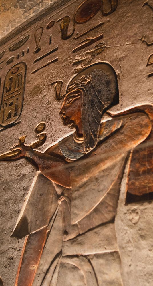 Intricate carving of an ancient Egyptian figure holding an offering with hieroglyphs in the background