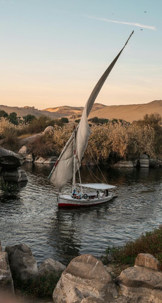 A traditional felucca sailing on a calm river surrounded by natural scenery and rocky formations