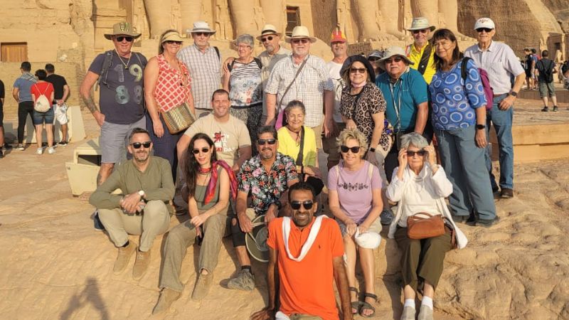 Tourists gathering in front of the majestic Abu Simbel Temples in Egypt, featuring large statues of Pharaoh Ramses II carved into the rock facade under a clear blue sky