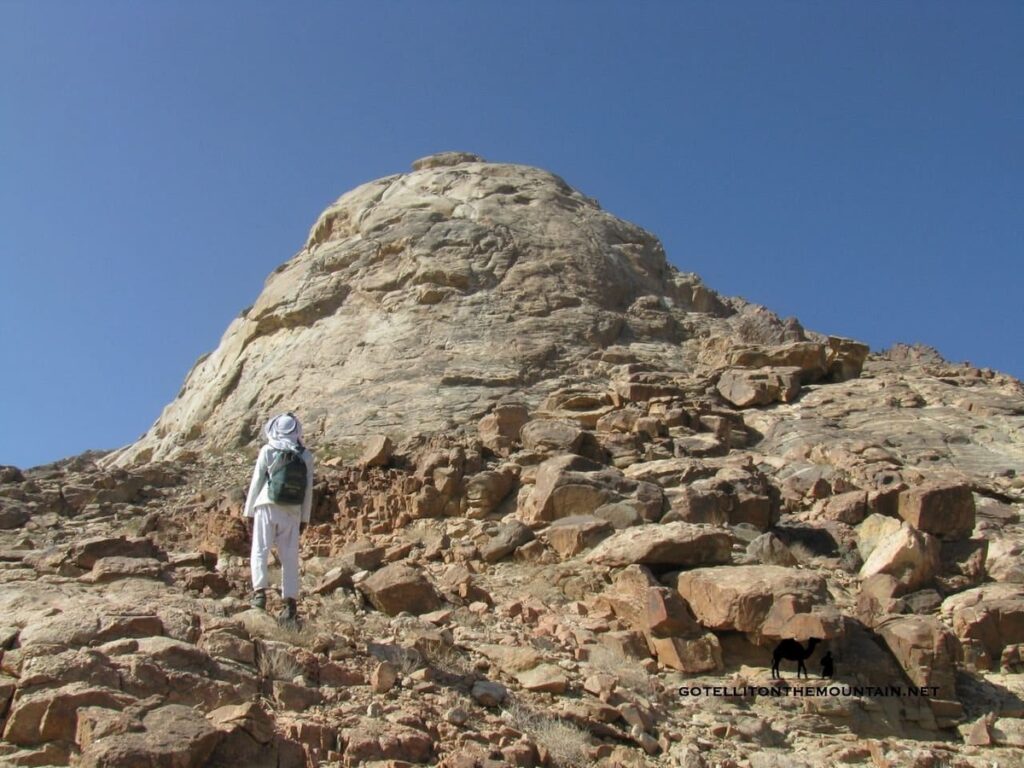 A lone hiker climbing the rocky trail of Jebel Salla in Wadi Feiran under a clear blue sky.