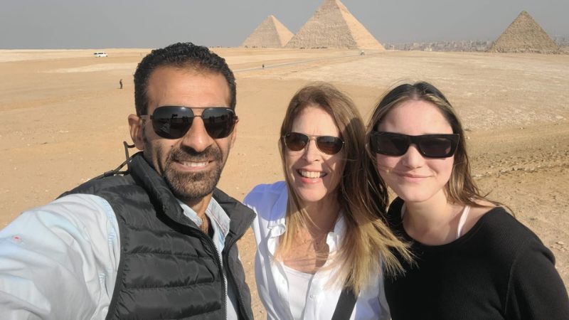 A group of smiling tourists taking a selfie with the Pyramids of Giza in the background