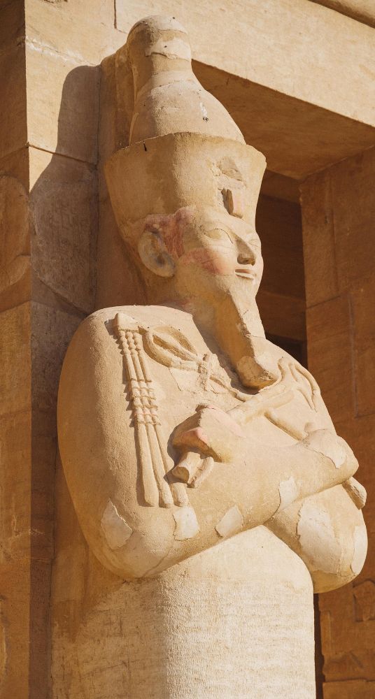 Statue of a pharaoh wearing a crown with crossed arms displayed on a sandstone wall