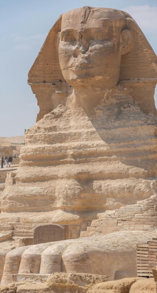 Side view of the Great Sphinx of Giza with a pyramid in the background against a clear blue sky