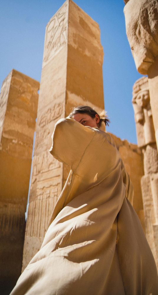 Woman posing in front of ancient Egyptian ruins with towering stone pillars under a bright sky