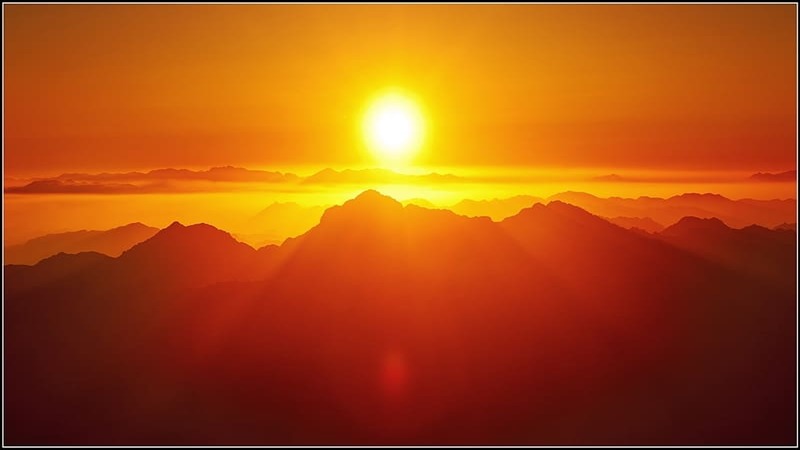 Sunrise over mountain peaks with golden hues illuminating the sky and clouds.