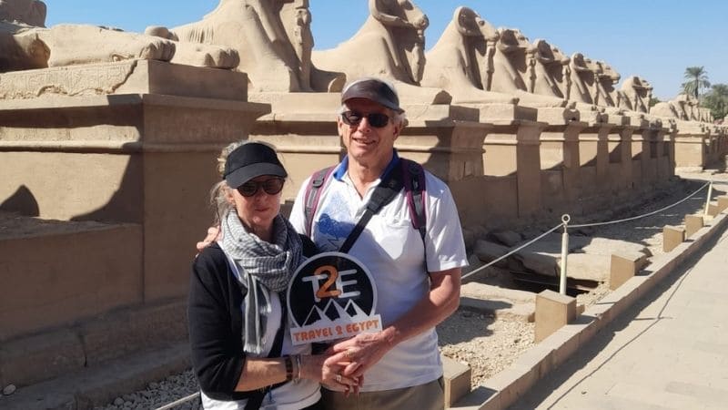 A couple walking along the Avenue of Sphinxes at Karnak Temple in Egypt surrounded by ancient sandstone statues under a bright sky