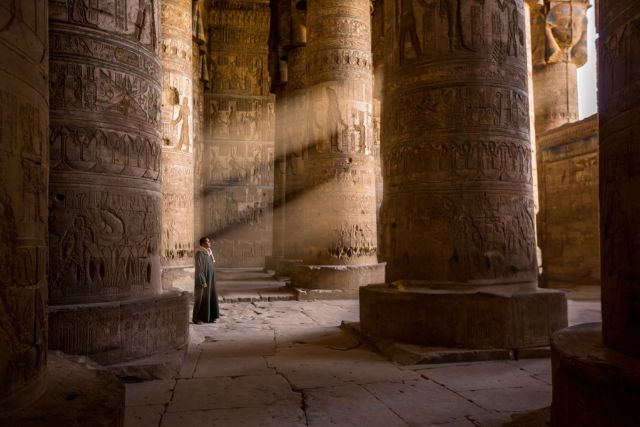 sunlit ancient Egyptian temple with towering columns and a person standing inside